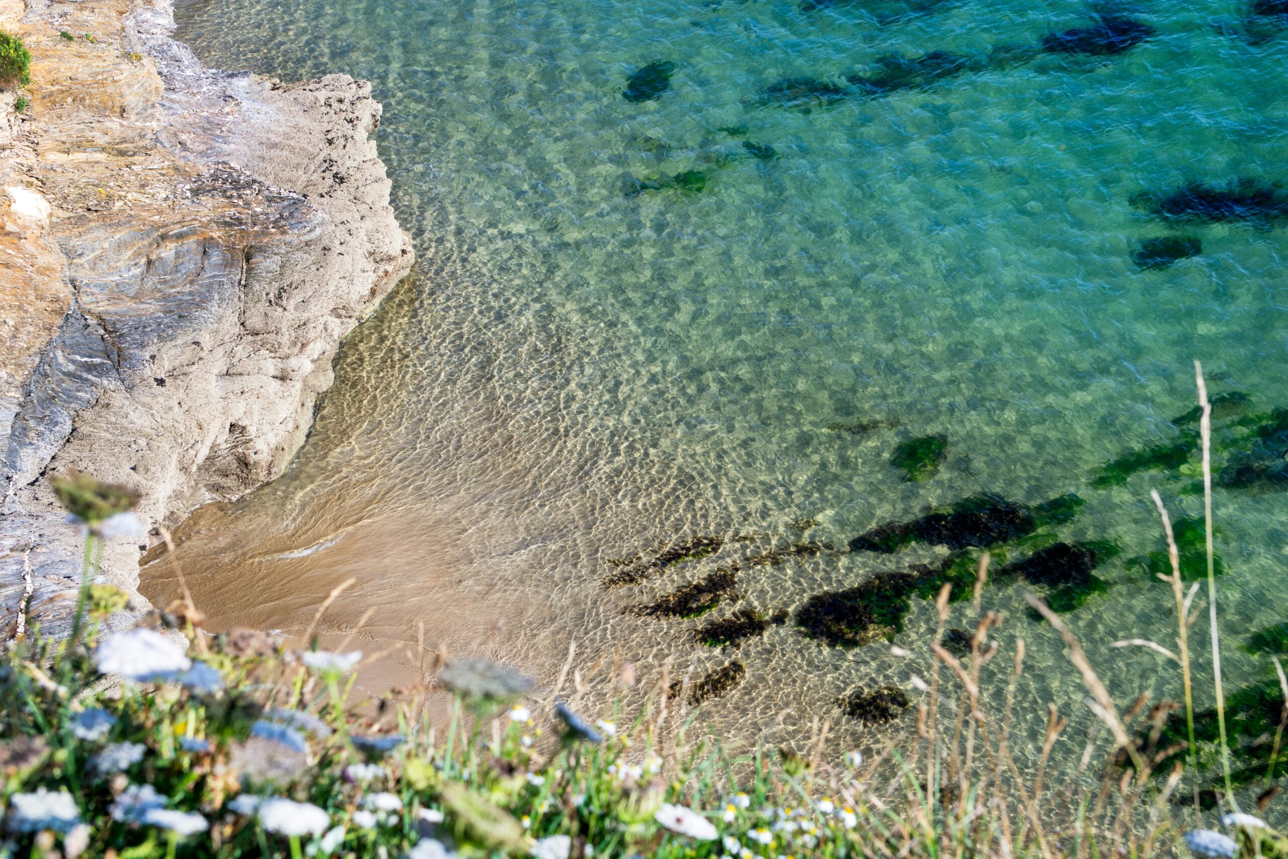 Stunning aerial view of Cornwall's rocky coastline and clear turquoise waters.